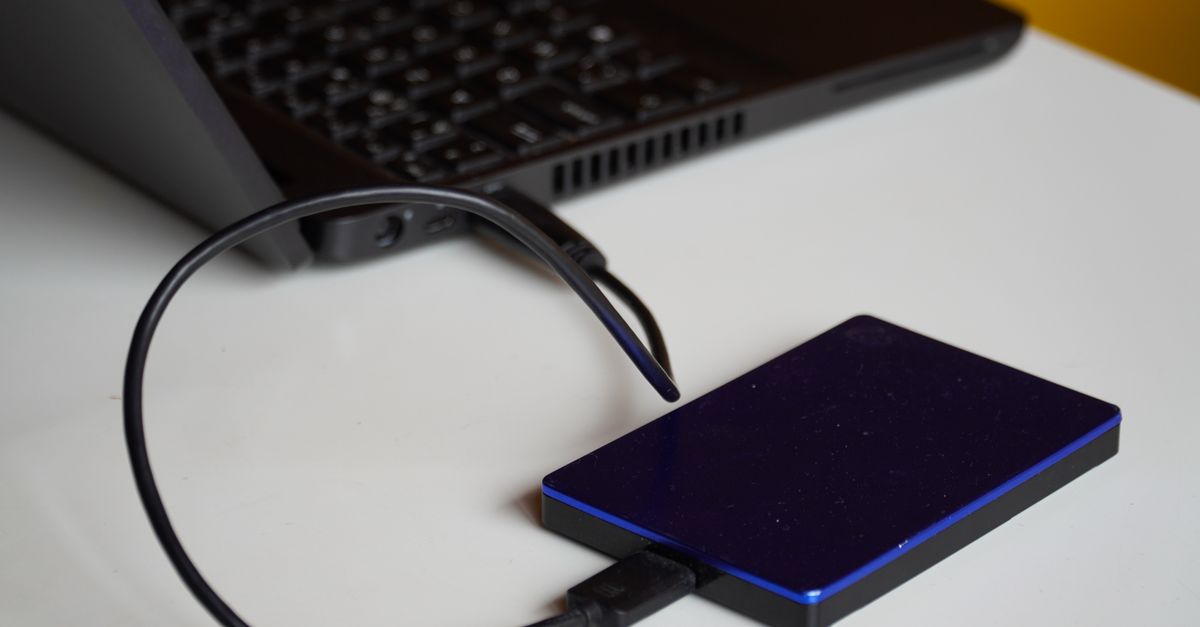 Disco duro externo junto a un portátil encendido en un escritorio